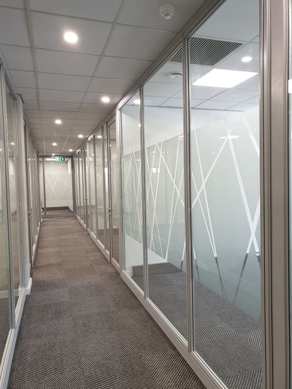 A Cliplok 54 office hallway featuring glass partitioning with frosted geometric patterns, providing a modern and private workspace design.