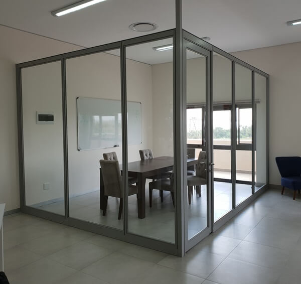 A Cliplok 54 low-level screen system with a glass enclosure and framed door, creating a semi-private meeting space within an open office layout.