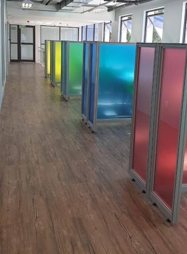 A Cliplok 54 low-level screen system featuring colorful frosted panels in blue, green, and red, adding a vibrant and structured division to the walkway.
